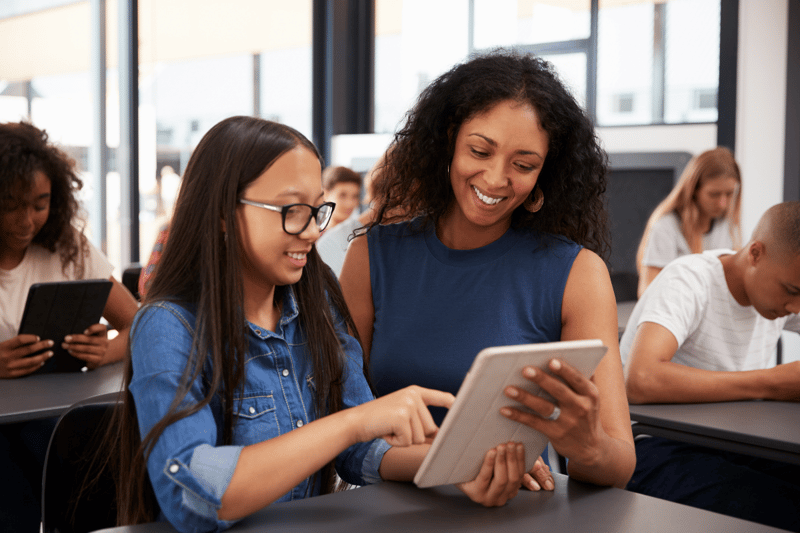 Female student and female teacher, both dressed in blue, looking at ipad together