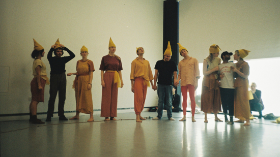 A group of actors standing in a line, all wearing tall hats, rehearsing a play.