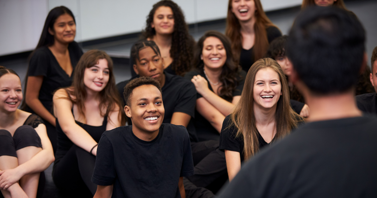 Theatre students dressed in black listening to teacher