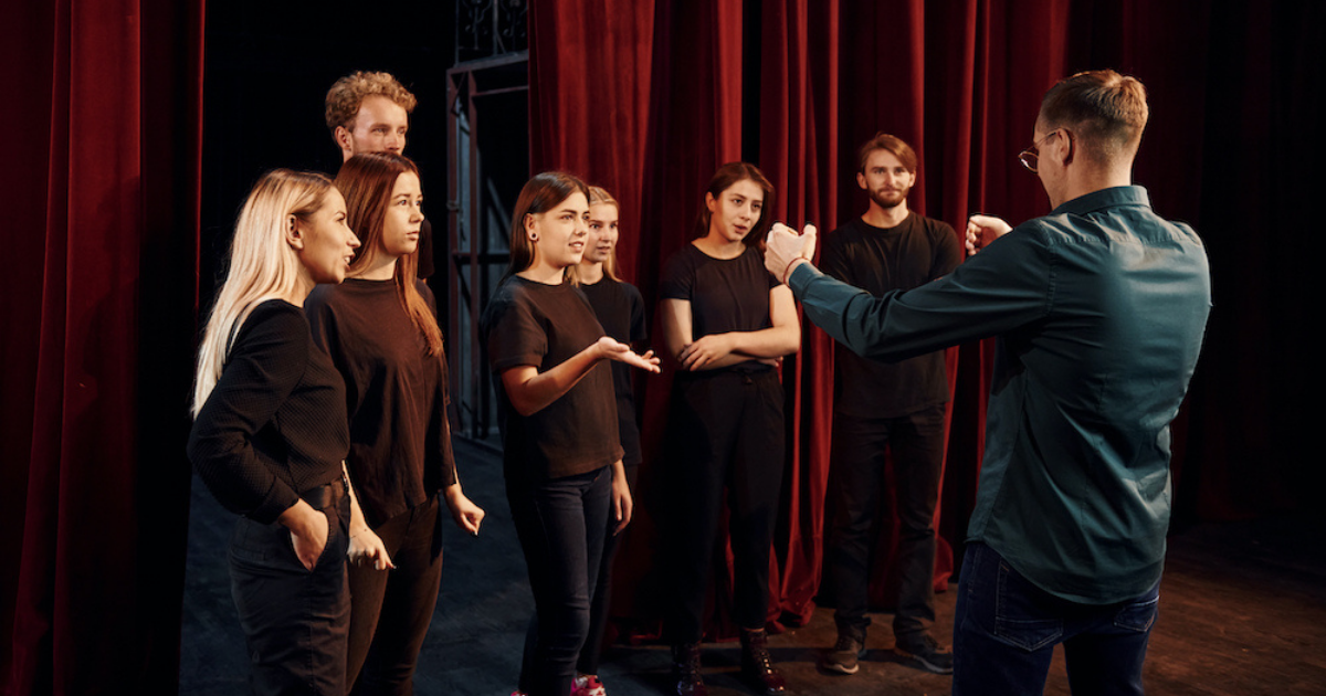 Drama students dressed in black listening to teacher