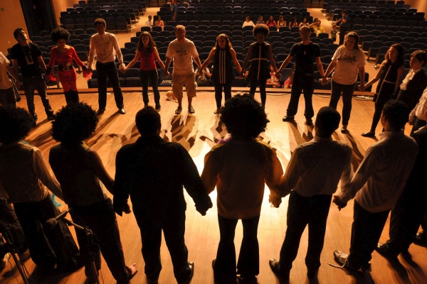 Group of theatre students holding hands in a circle on stage