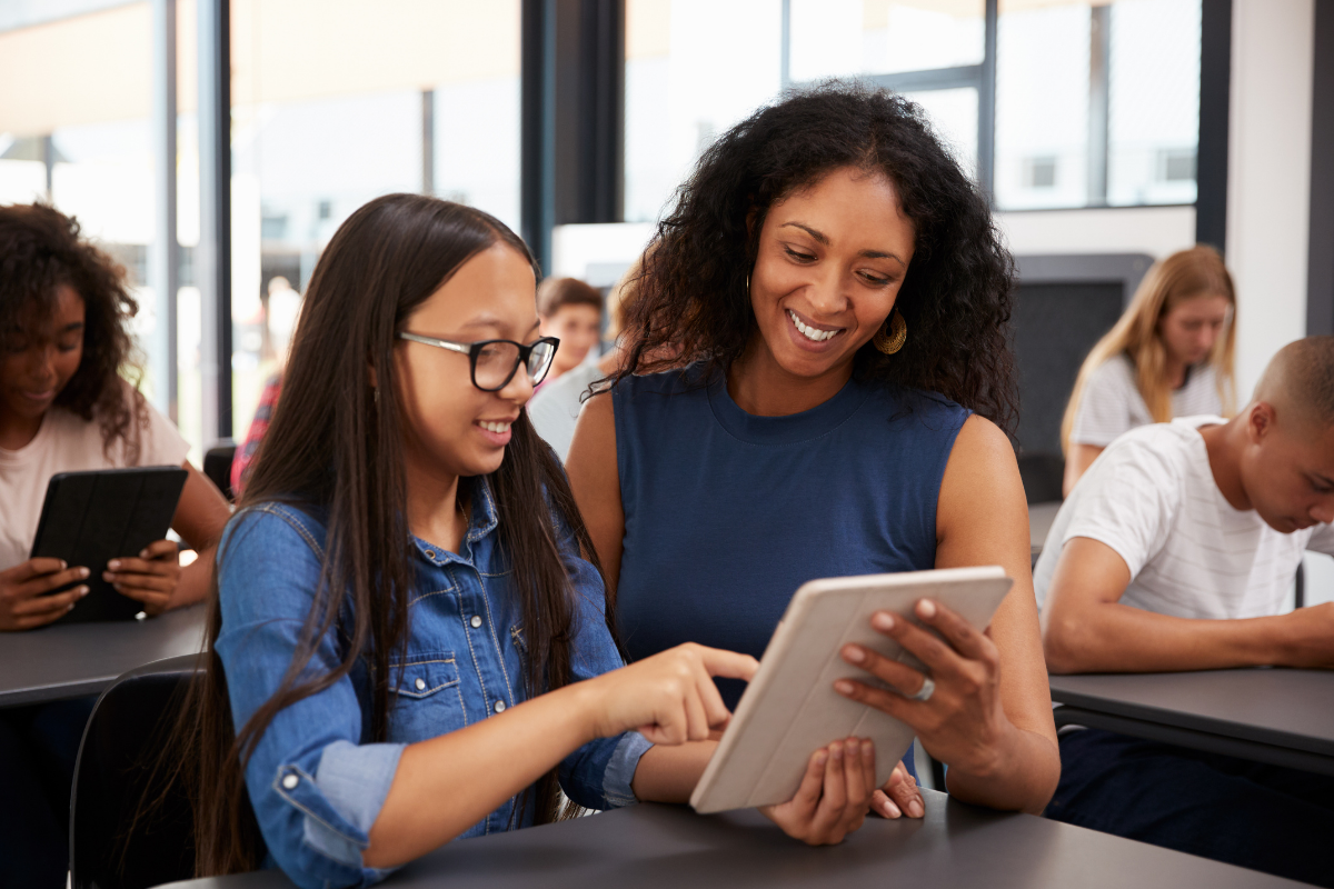 Female teacher and female student, both dressed in blue, looking at ipad 