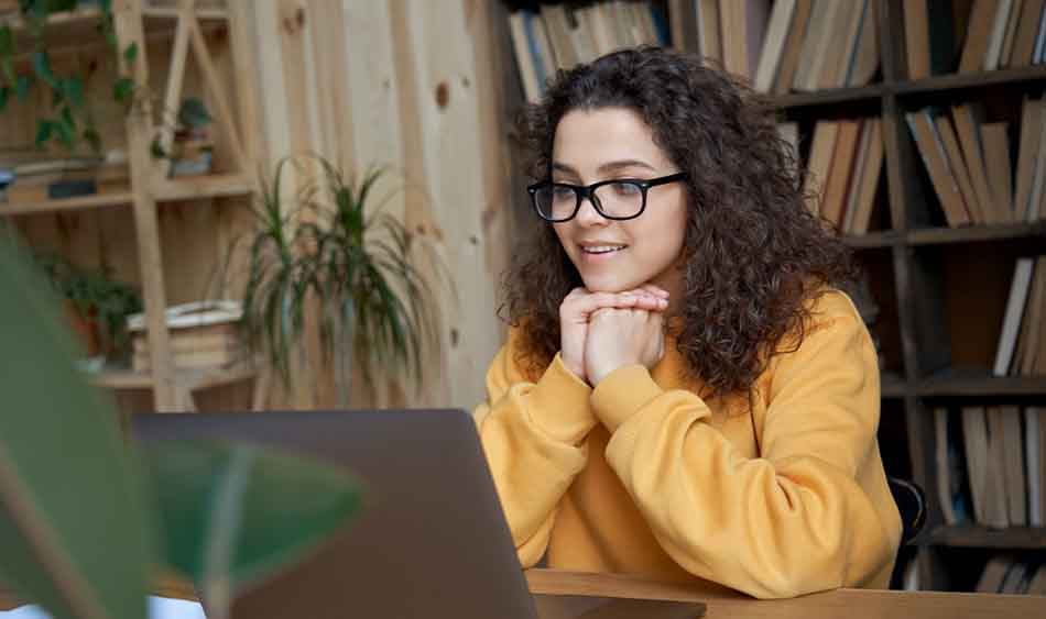 Female student with curly hair and yellow jumper looking at laptop screen